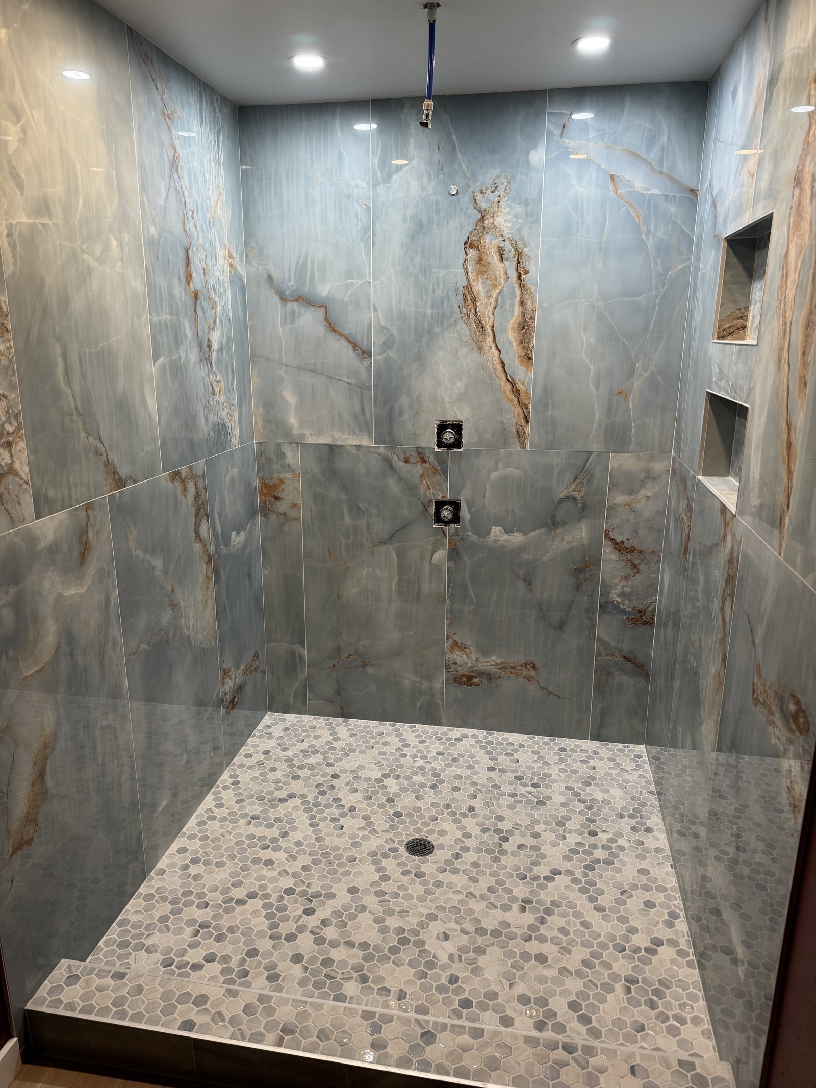 Custom onyx-tile master shower with hexagonal mosaic floor